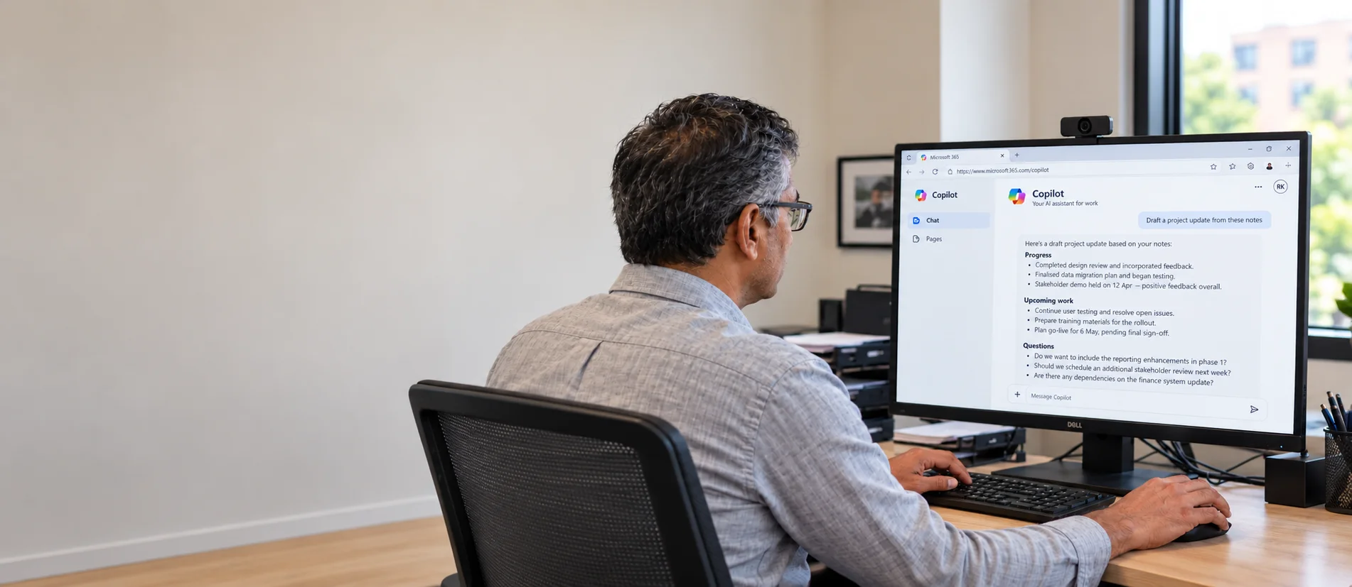 Professional using Copilot to draft a project update at an office workstation.